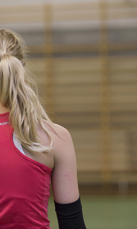 Tjej i sporthallen, i bakgrunden en tjej med volleyboll.