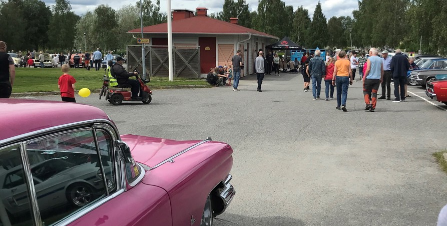 Bild från evenemanget Världens Fest sommaren 2022 som visar bilutställningen på parkeringen vid kommunhuset med många besökare och soligt väder.