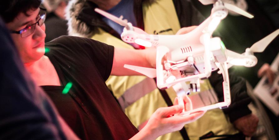 Ung person håller i och tittar på drönare i folkmassa. 